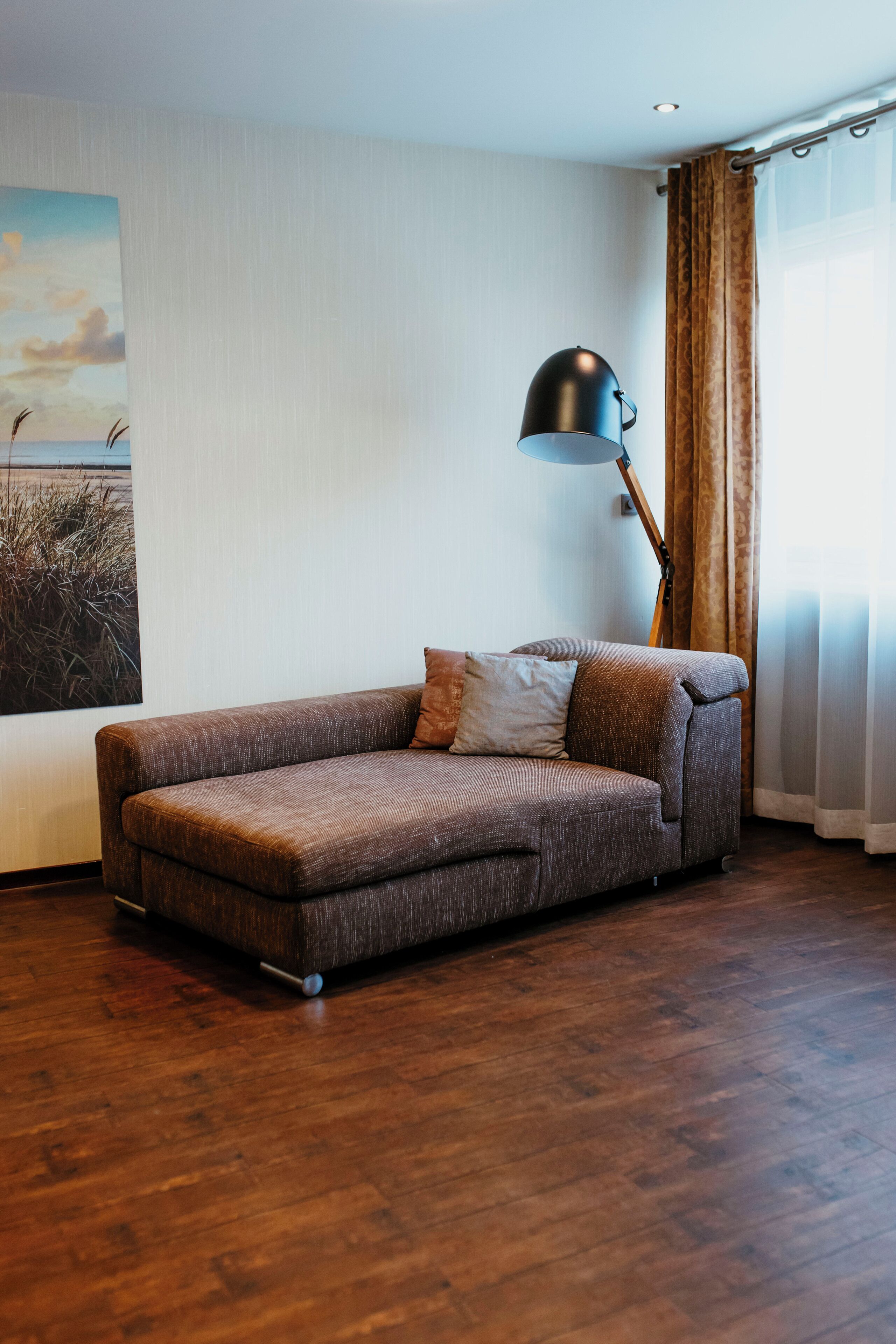 Un salon moderne avec un canapé d’angle, une lampe sur pied et un grand tableau accroché au mur.