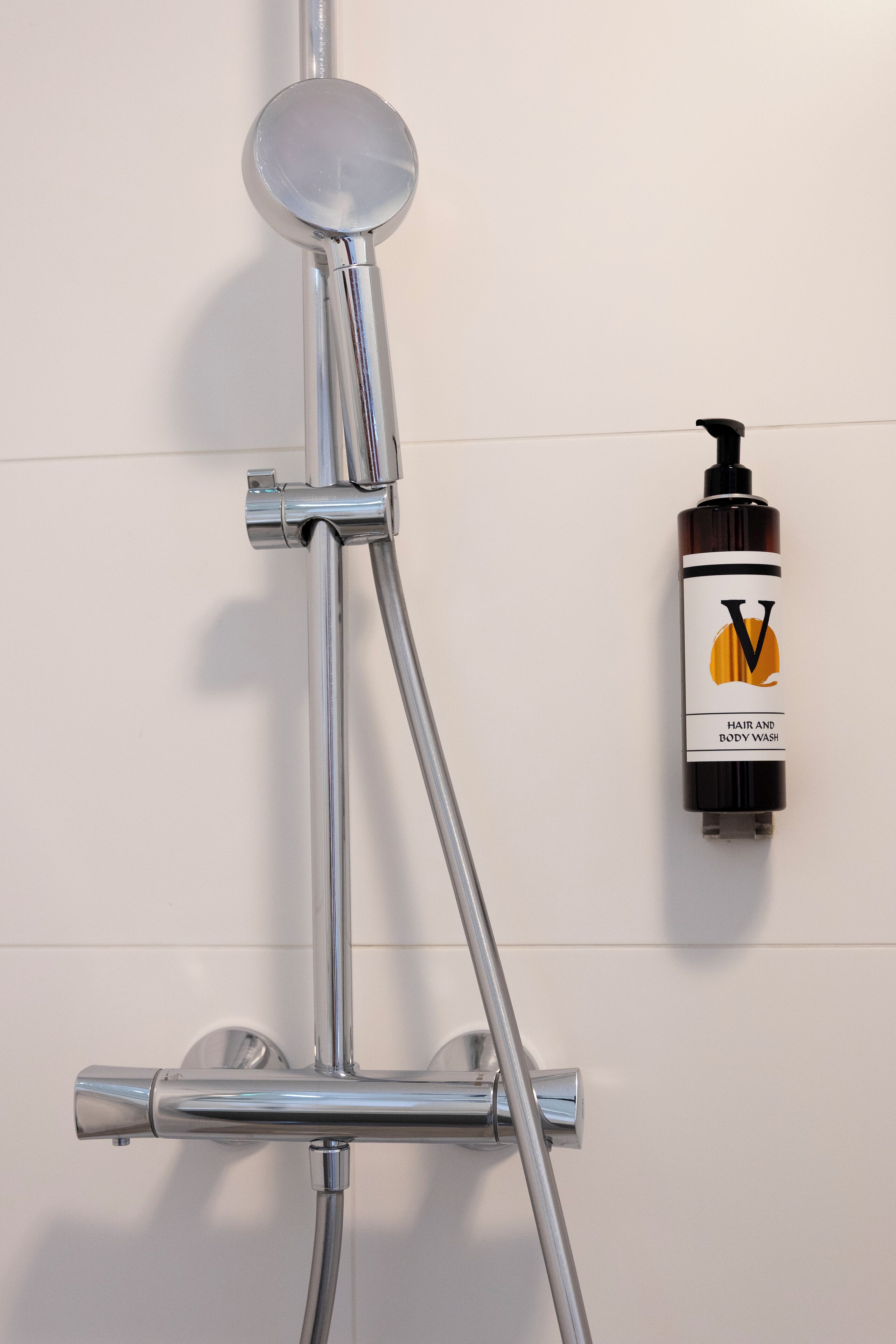 A chrome showerhead mounted on a wall, with a bottle of hair and body wash labeled 'V' to the right.