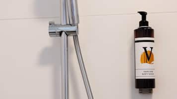 A chrome showerhead mounted on a wall, with a bottle of hair and body wash labeled 'V' to the right.