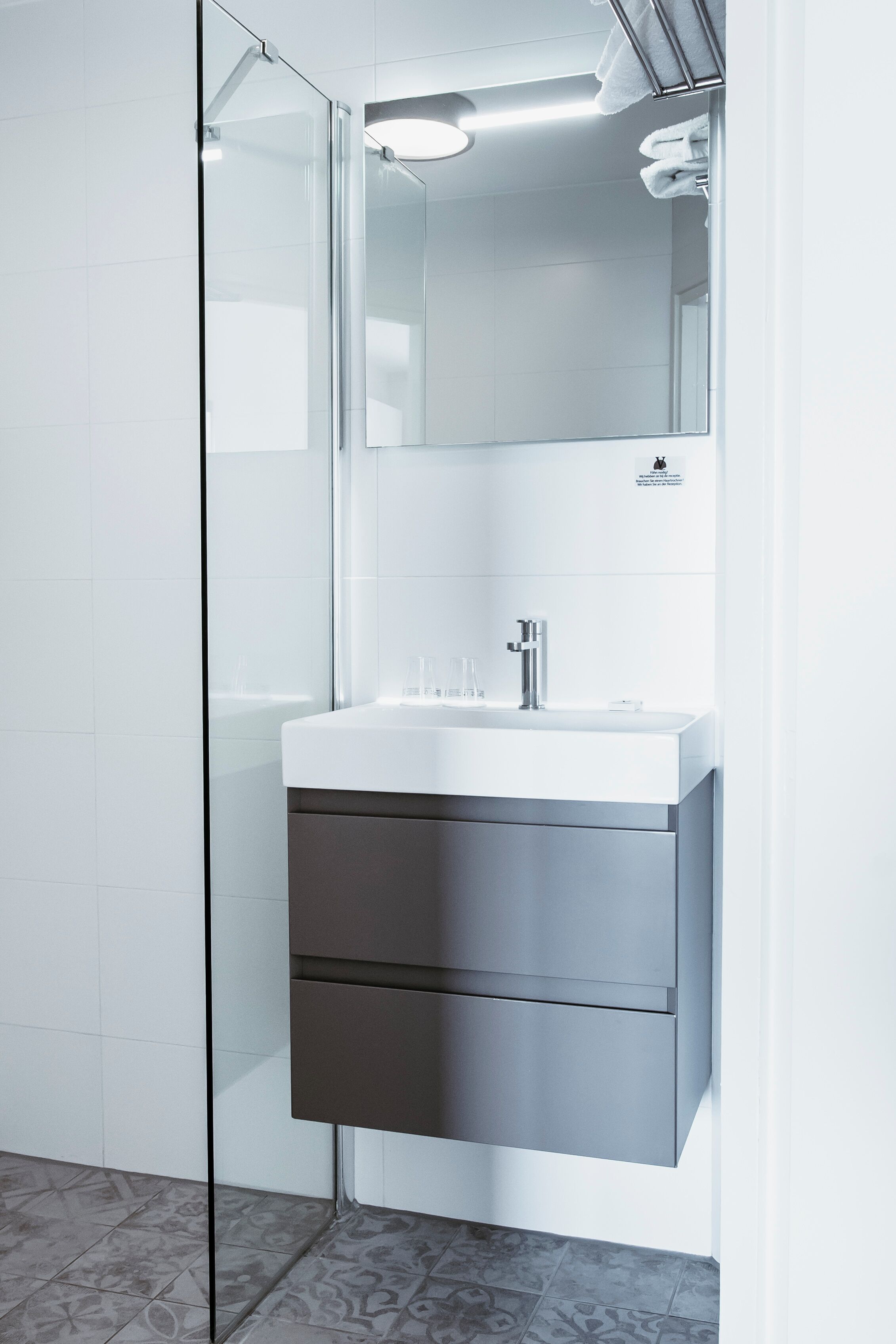 A modern bathroom with a glass shower enclosure, a white sink with a chrome faucet, and a dark-toned cabinet below.