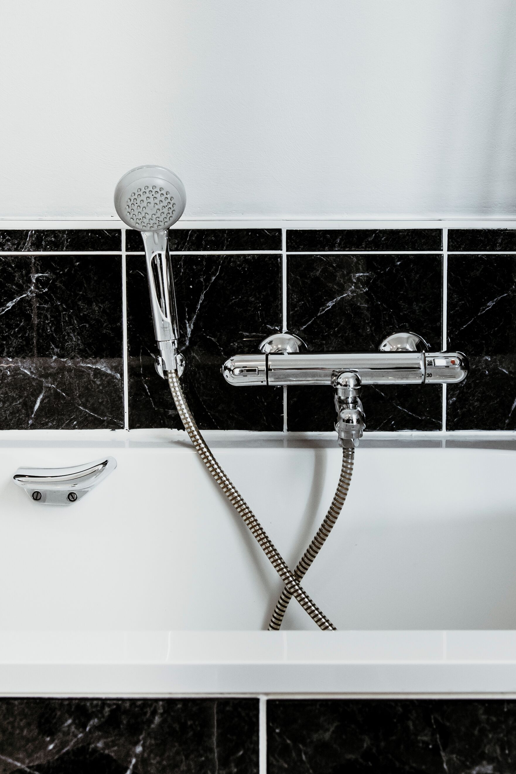 A bathroom with a white bathtub, a handheld showerhead, and a wall-mounted faucet.