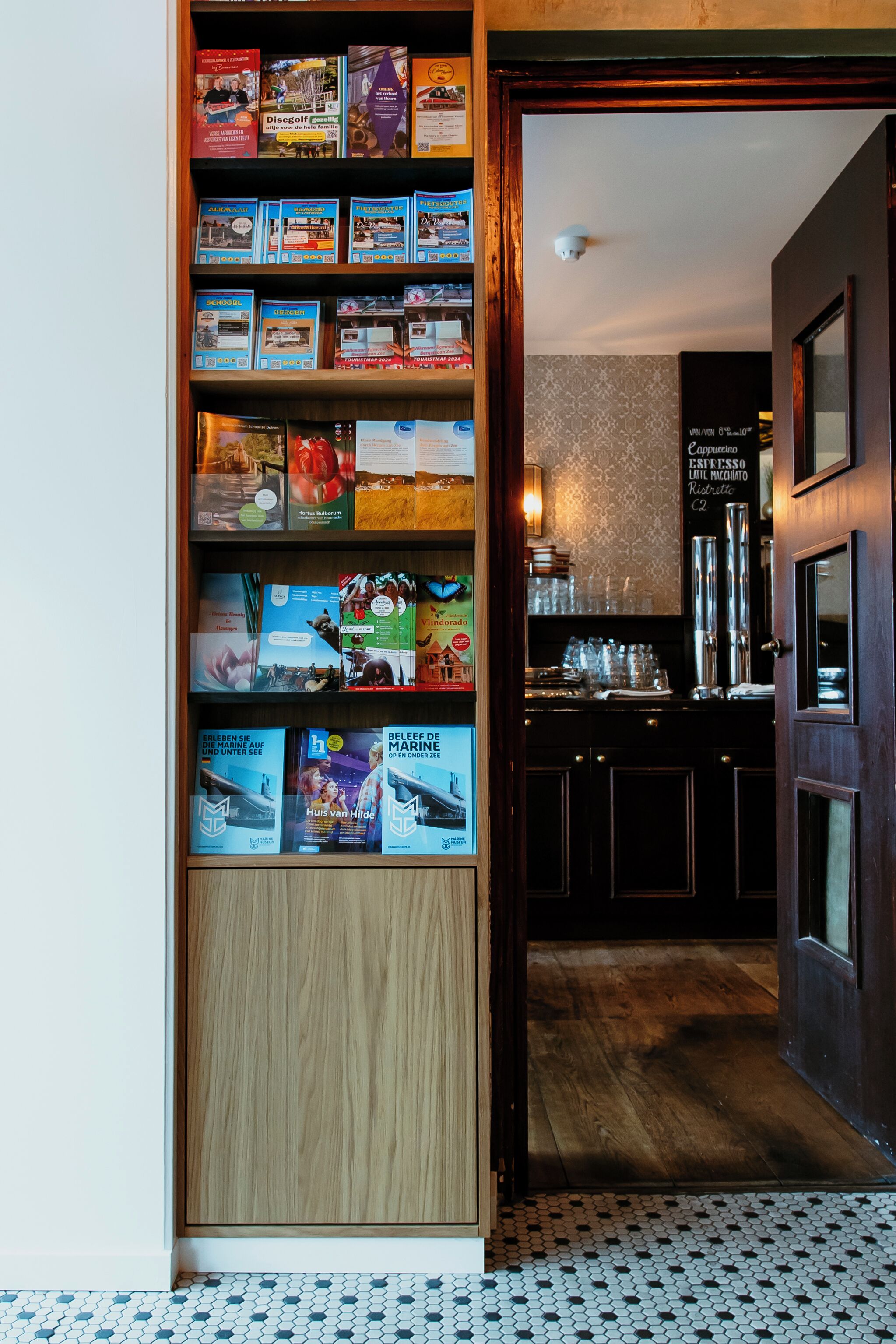 Ein Flur mit Bücherregal voller Bücher und Zeitschriften, der zu einer Küchenzeile mit Kaffeemaschine und einer Kreidetafel-Speisekarte führt.