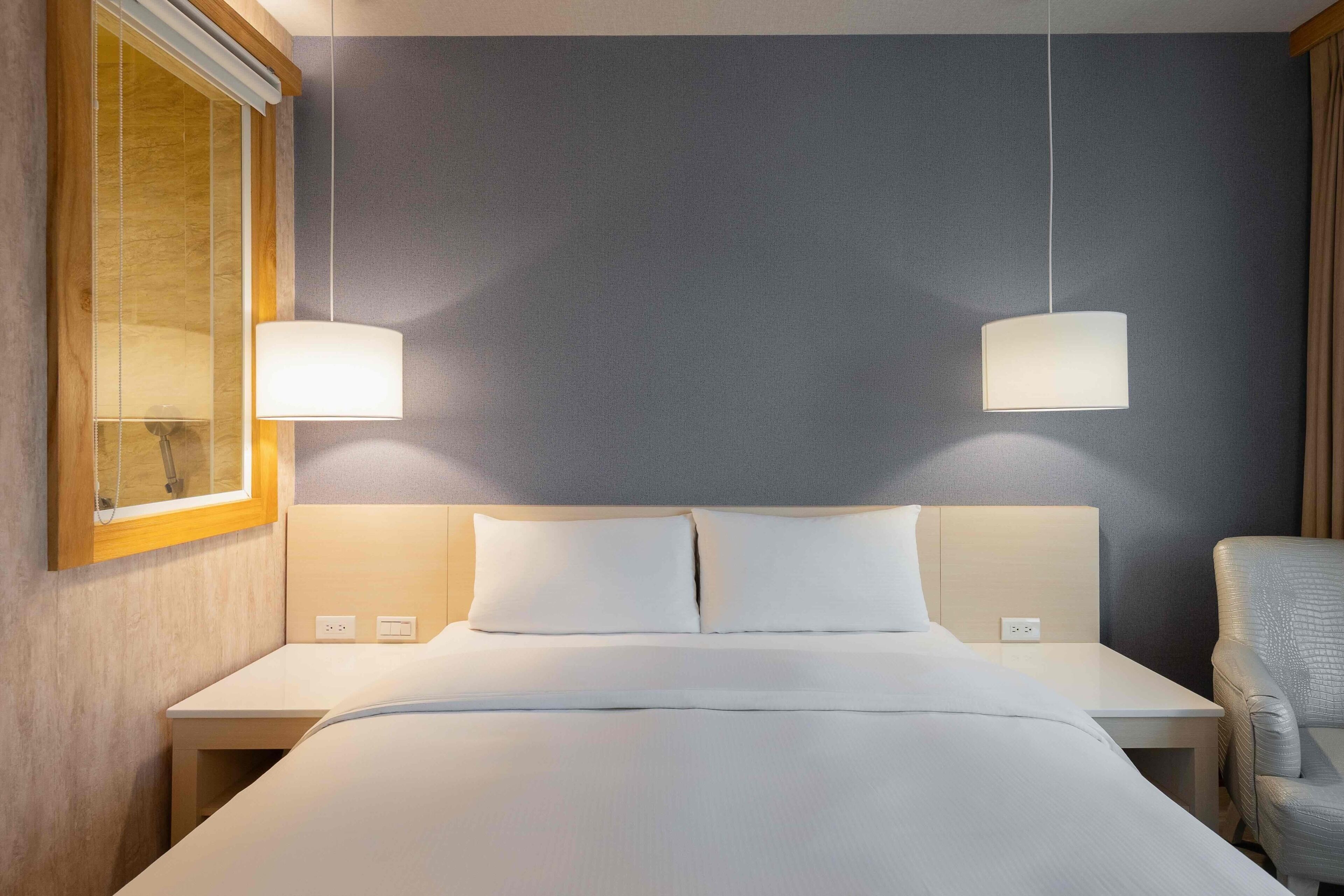 A hotel room with a bed, bedside tables, lamps, and a chair.