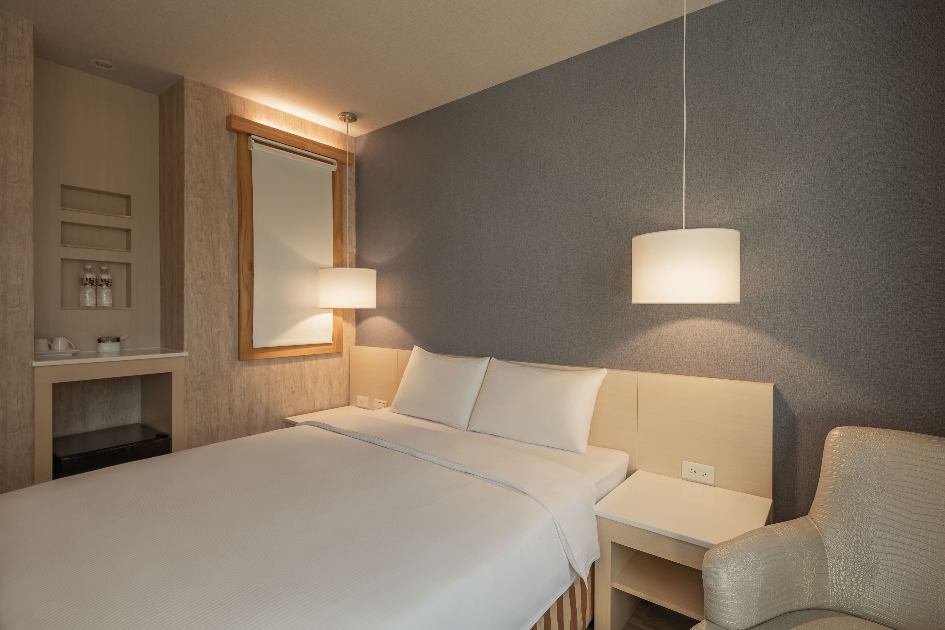 Habitación de hotel con cama, mesitas de noche, una silla, un espejo y un estante con artículos de aseo.