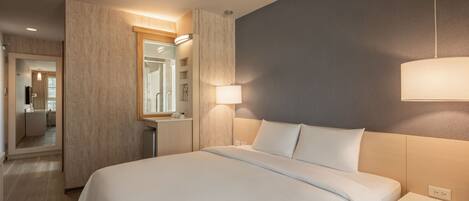 Una habitación de hotel con una cama grande, mesitas de noche, un espejo y una lámpara de pared.