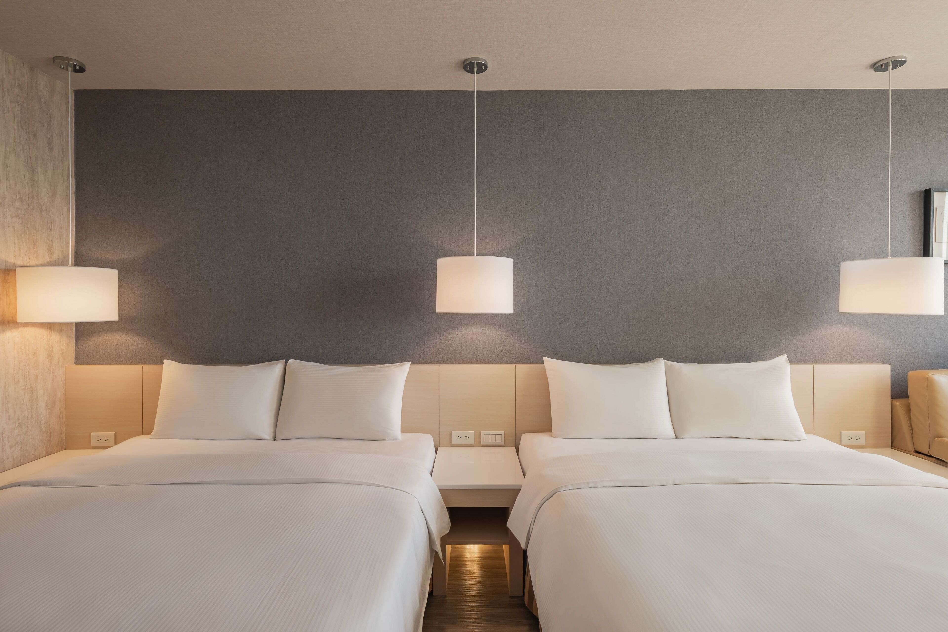 Ein Hotelzimmer mit zwei Betten, einer neutralen Farbgestaltung und modernen Leuchten.