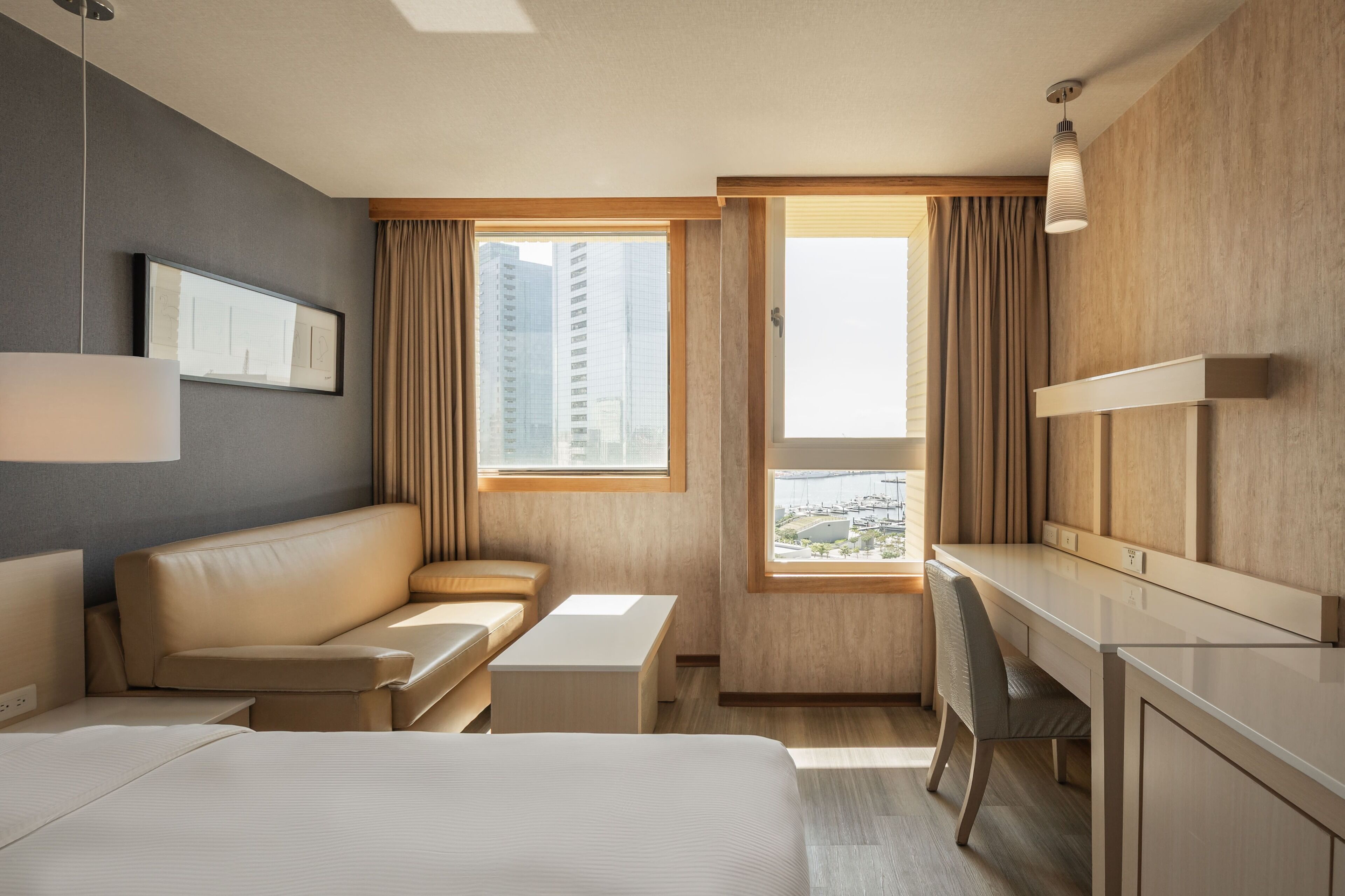 Quarto de hotel moderno com cama, sofá, escrivaninha e vista para a cidade.