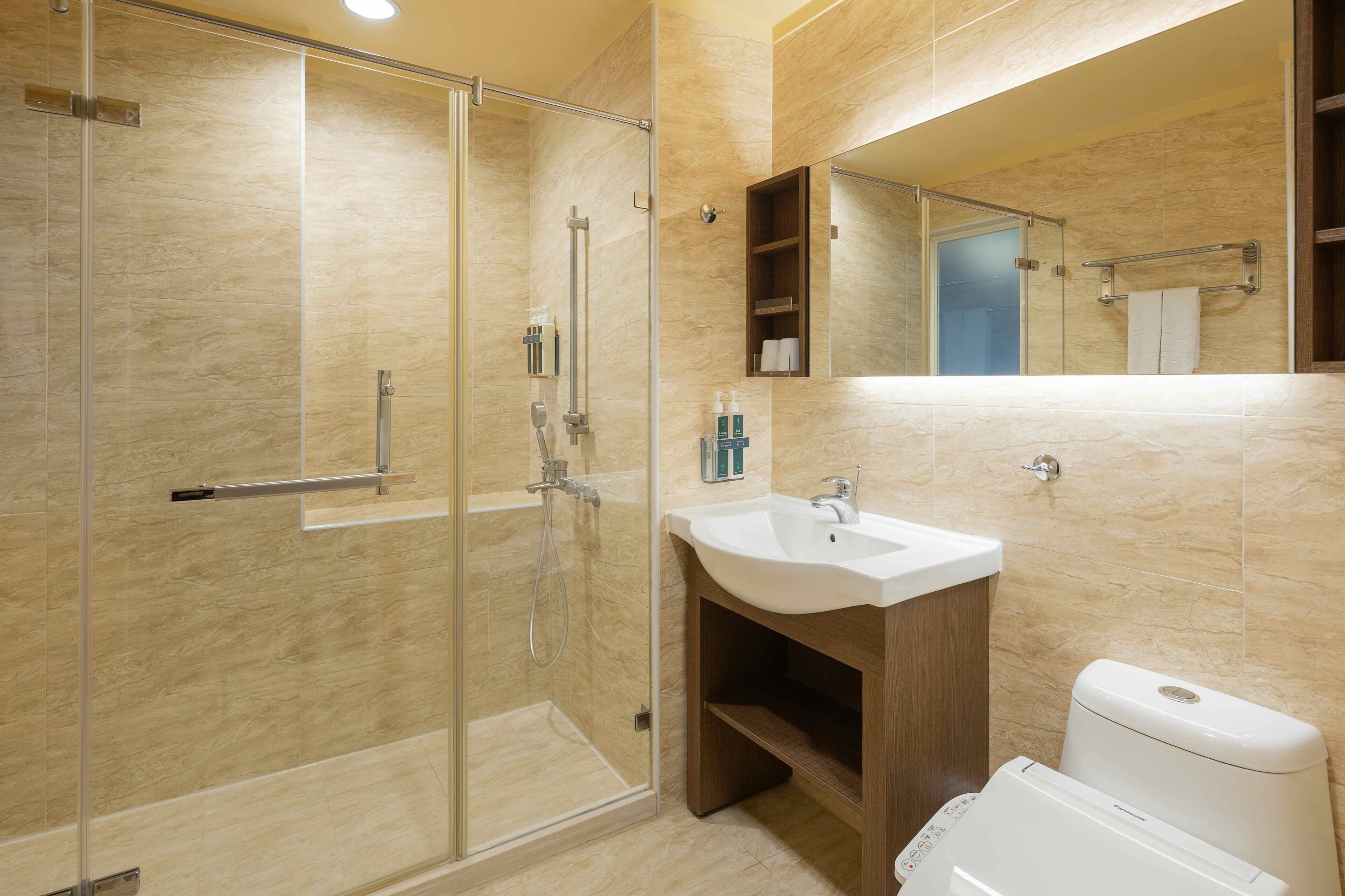 Un baño moderno con cabina de ducha de vidrio, un lavamanos con tocador de madera y un inodoro.