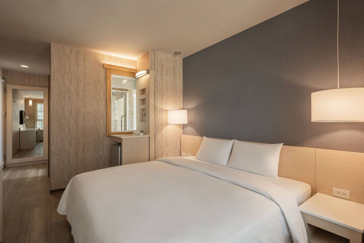 Una habitación de hotel con una cama grande, mesitas de noche, un espejo y una lámpara de pared.
