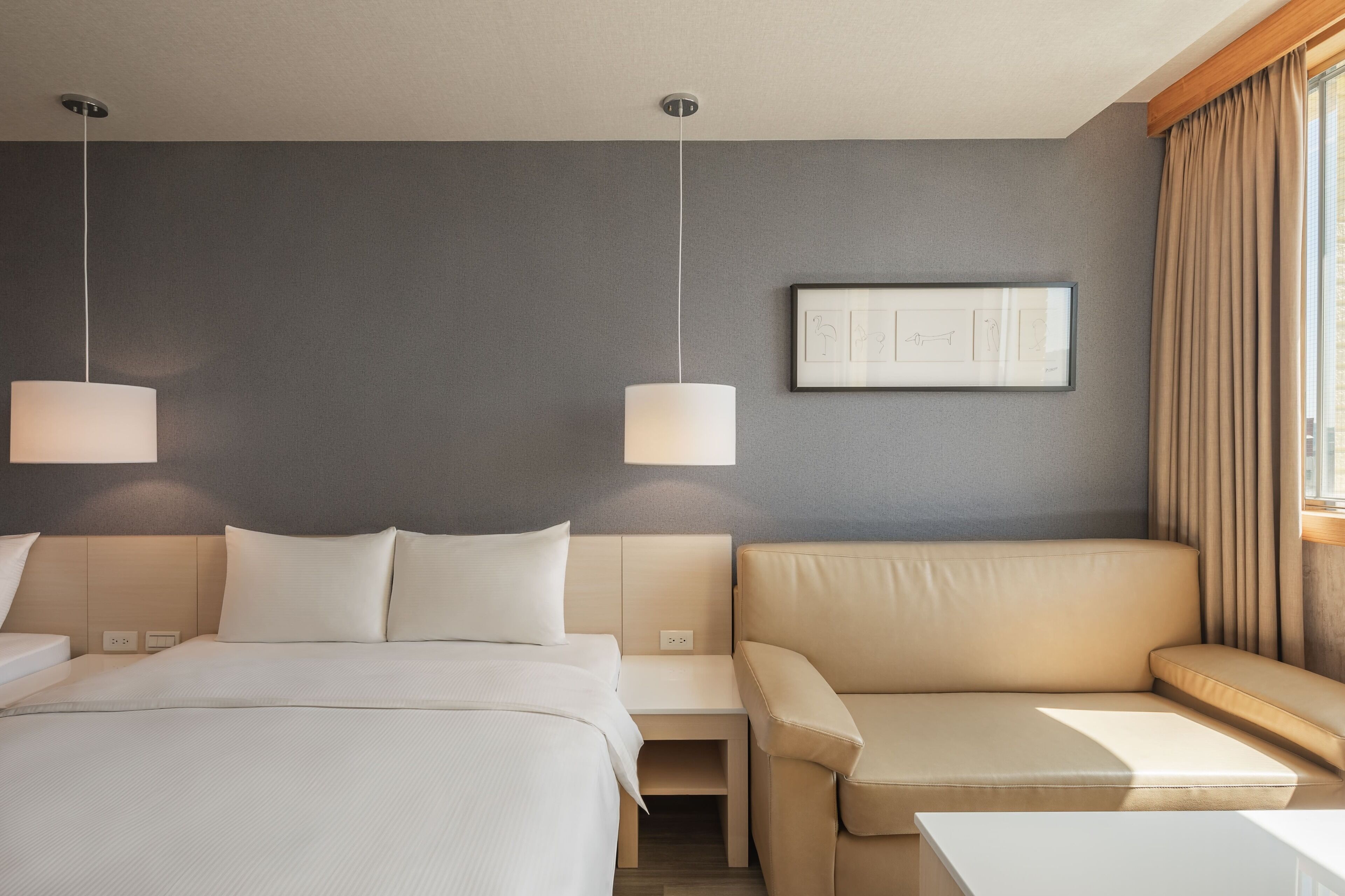 A hotel room with a bed, a sofa, a small table, and a wall-mounted picture.