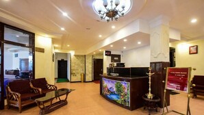 A lobby with a reception desk, a television, a chandelier, and seating area. - Anand Palace Hotel (Udaipur)
