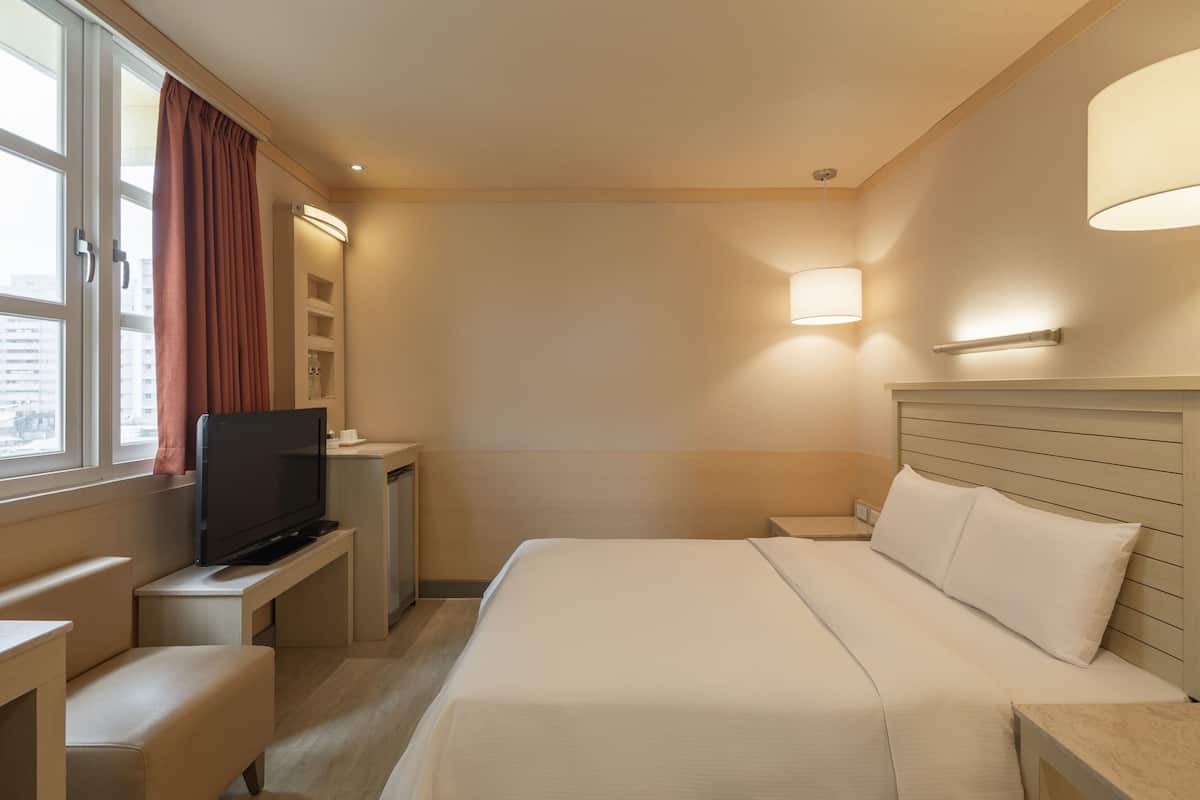 Ein Hotelzimmer mit Bett, Fernseher auf einem Tisch, Schreibtisch und einem Fenster mit Vorhängen.