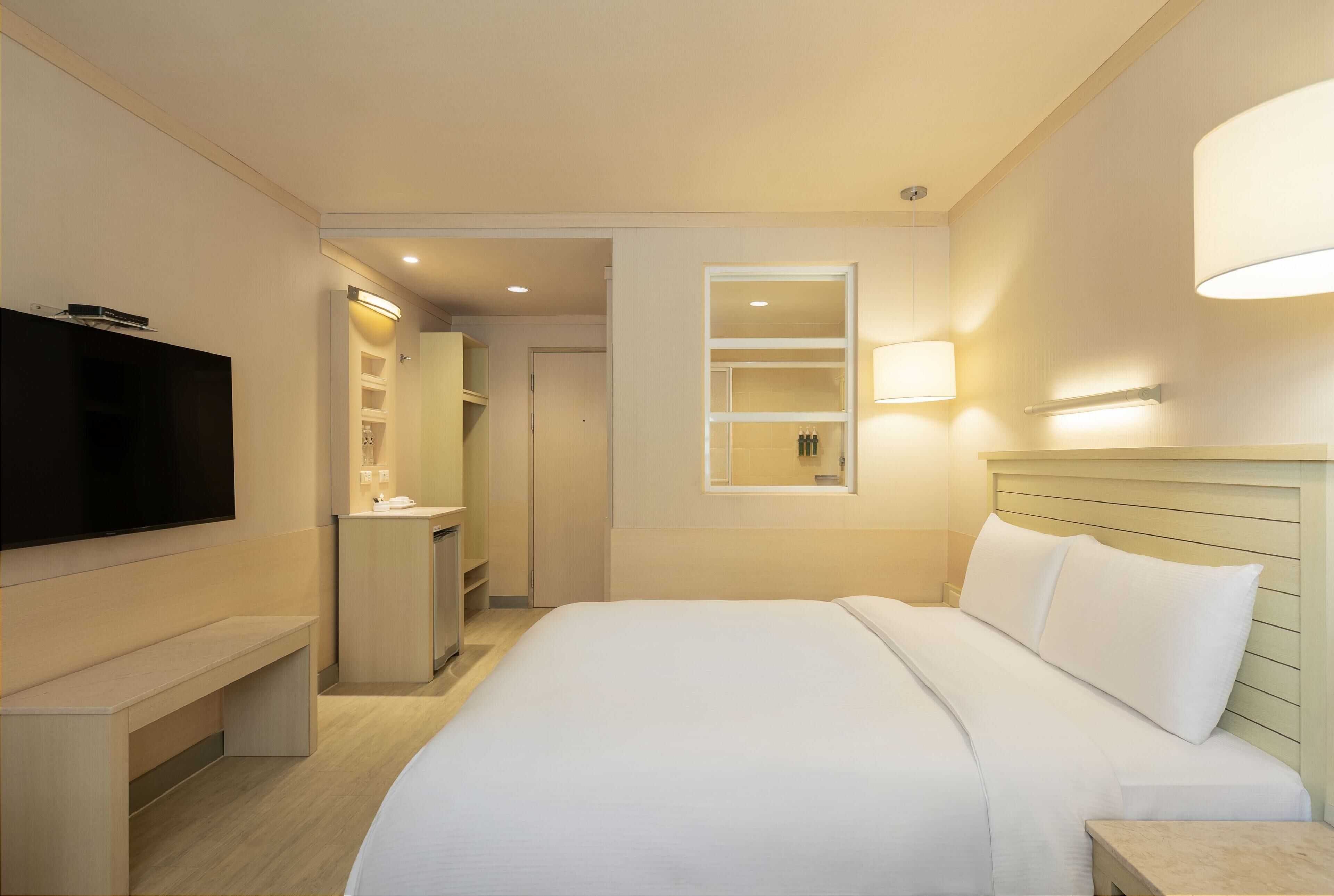 A hotel room with a bed, a TV, a desk, a mirror, and a bathroom.