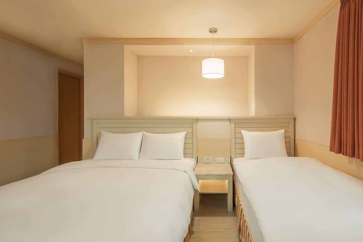 Ein Hotelzimmer mit zwei Betten, einem Nachttisch, einer Lampe und einem Fenster mit Vorhängen.
