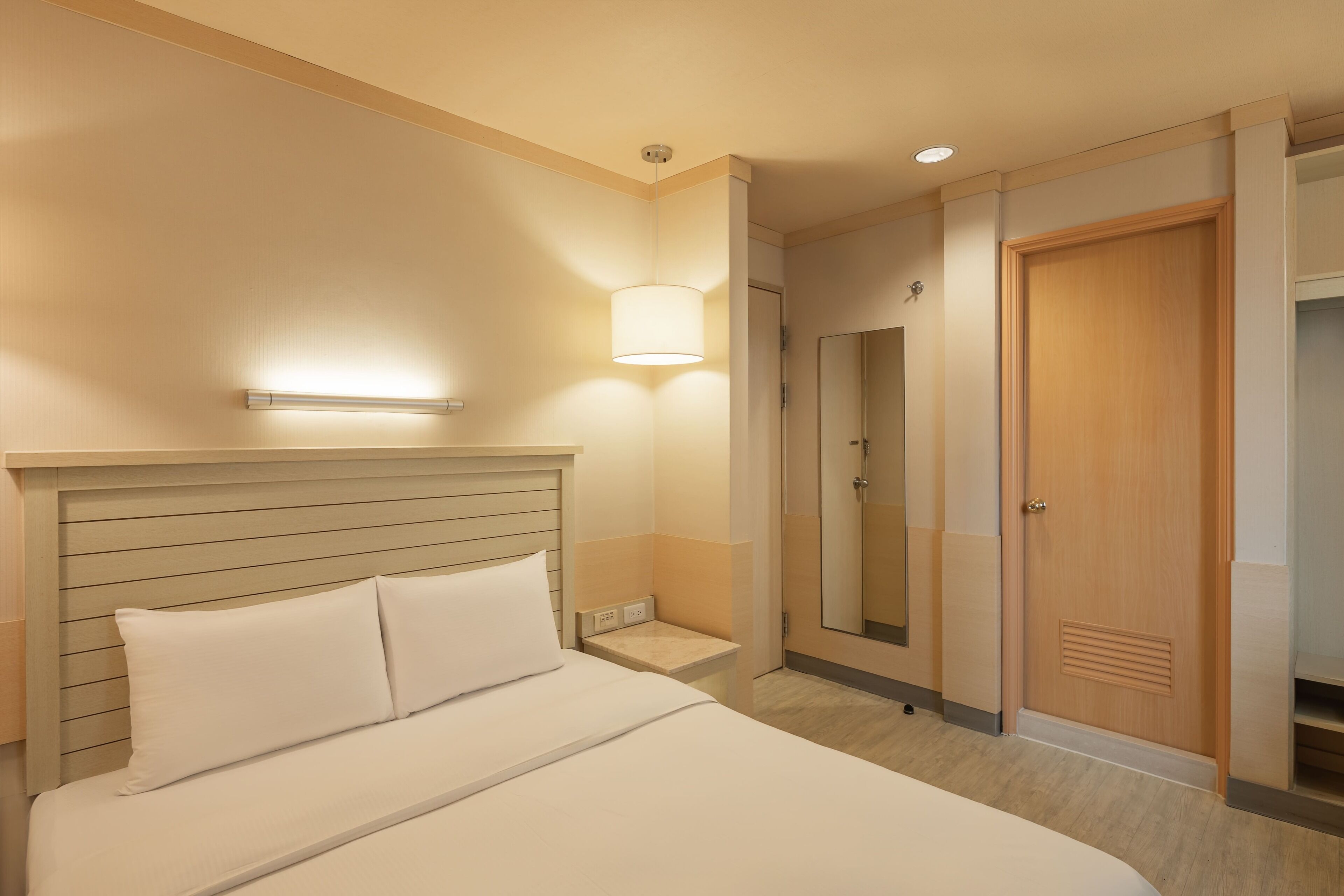 Une chambre d’hôtel avec un lit, une lampe de chevet et une porte donnant sur une salle de bain.