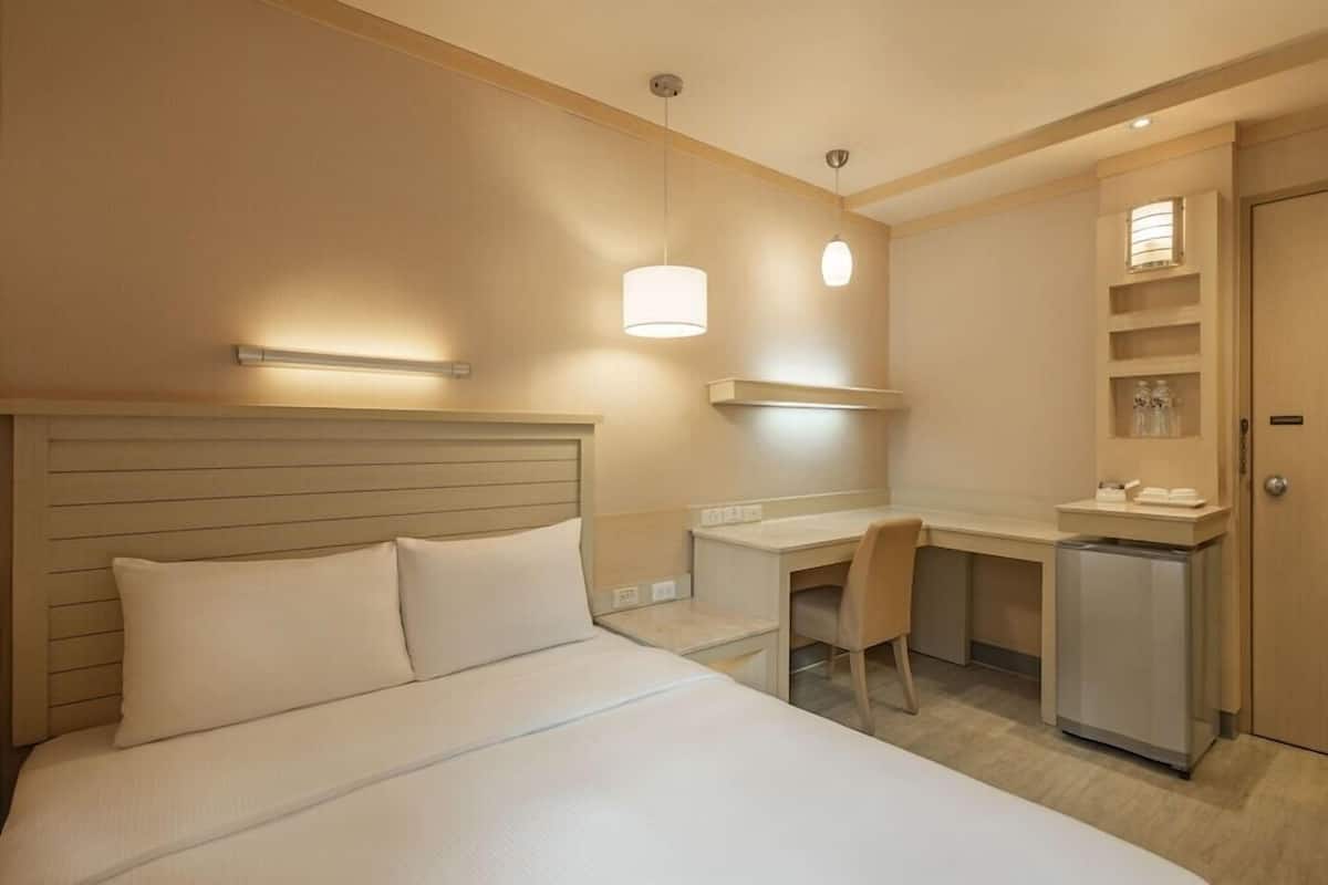 Ein Hotelzimmer mit Bett, Schreibtisch, Stuhl und einem kleinen Kühlschrank.