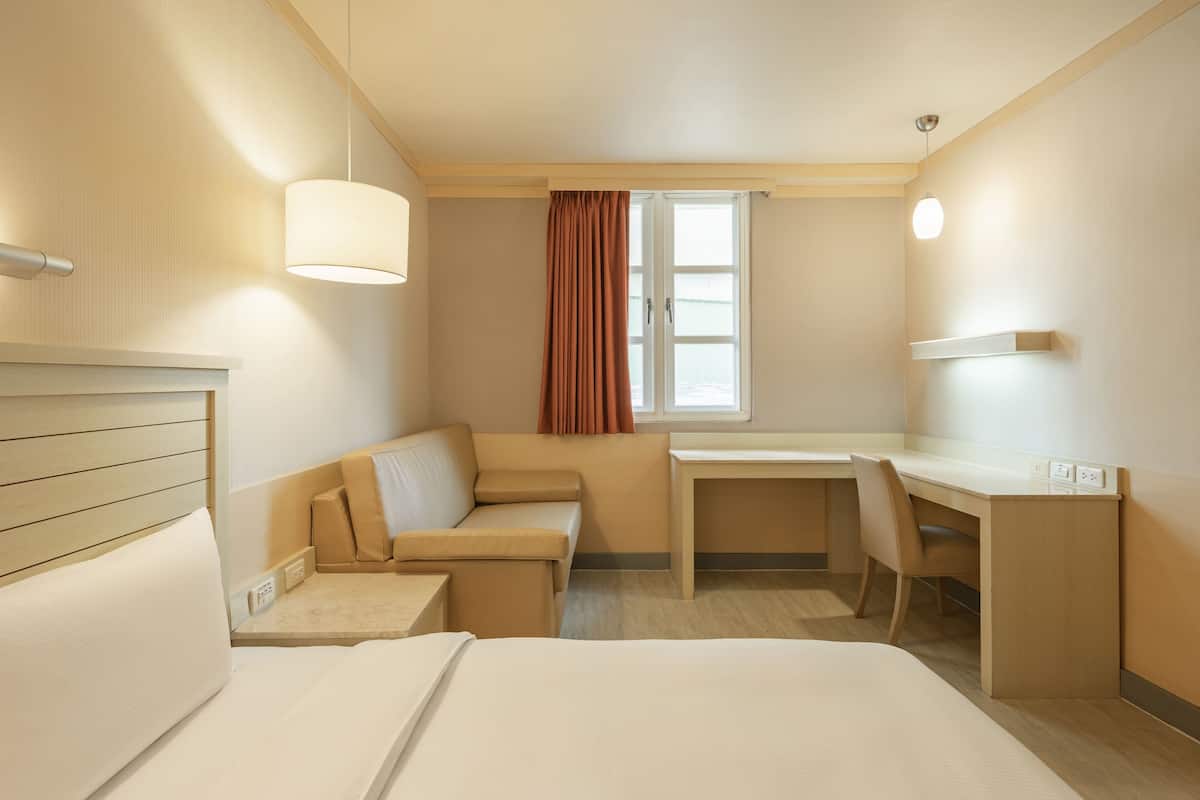 Ein Hotelzimmer mit Bett, Sofa, Schreibtisch und einem Fenster mit Vorhängen.