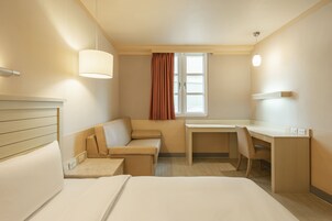 Camera d'albergo con un letto, una poltrona, una scrivania e una finestra con tende.