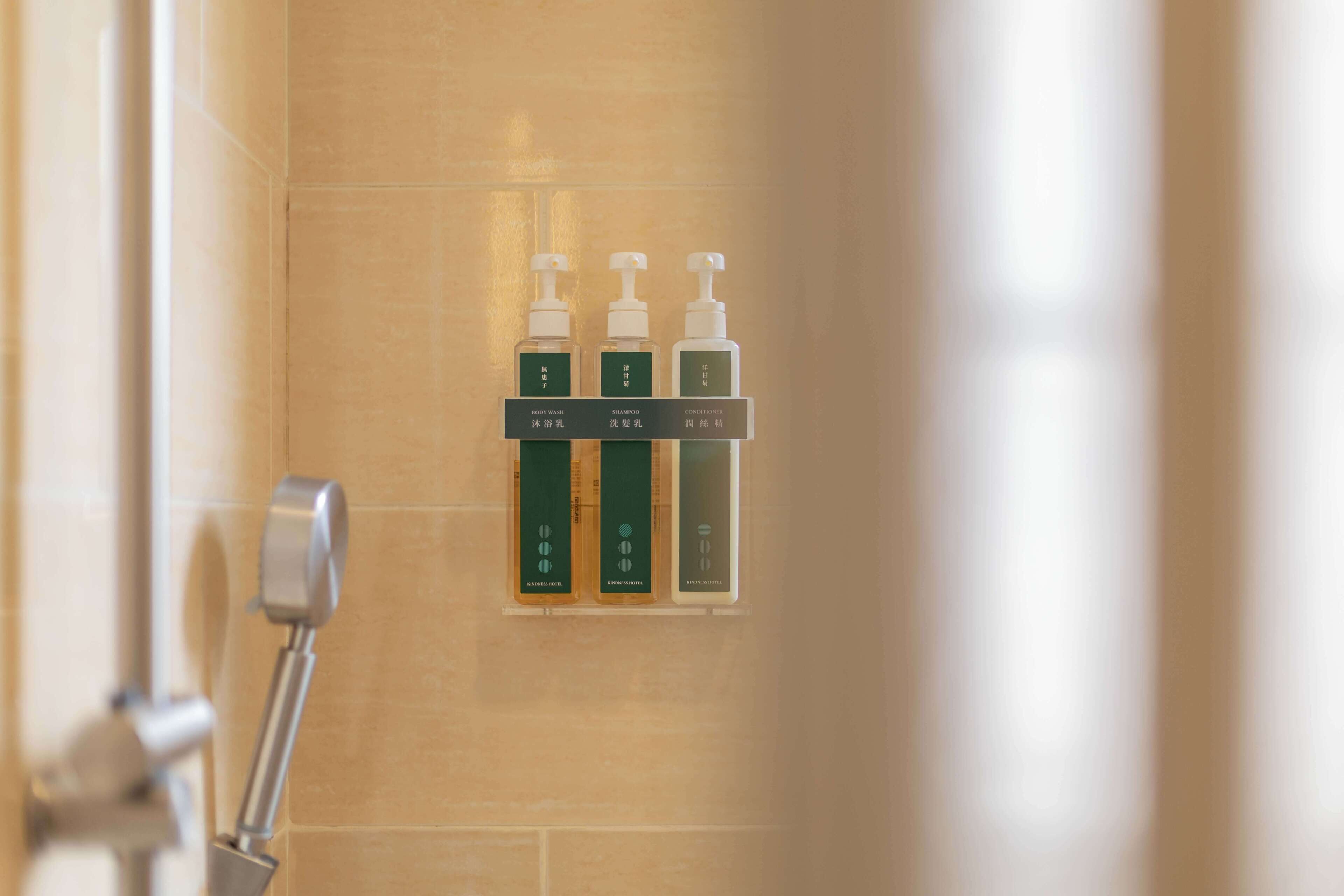 Dispensador mural con tres botellas etiquetadas para gel de ducha, champú y acondicionador.