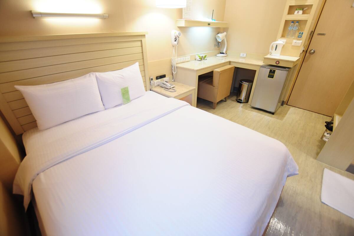 Ein Hotelzimmer mit Bett, Schreibtisch, Minikühlschrank, Telefon und Mülleimer.