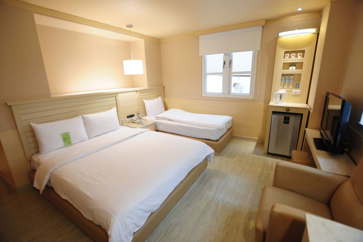 Une chambre d’hôtel avec deux lits, un bureau, un réfrigérateur, une télévision et une fenêtre avec des stores.