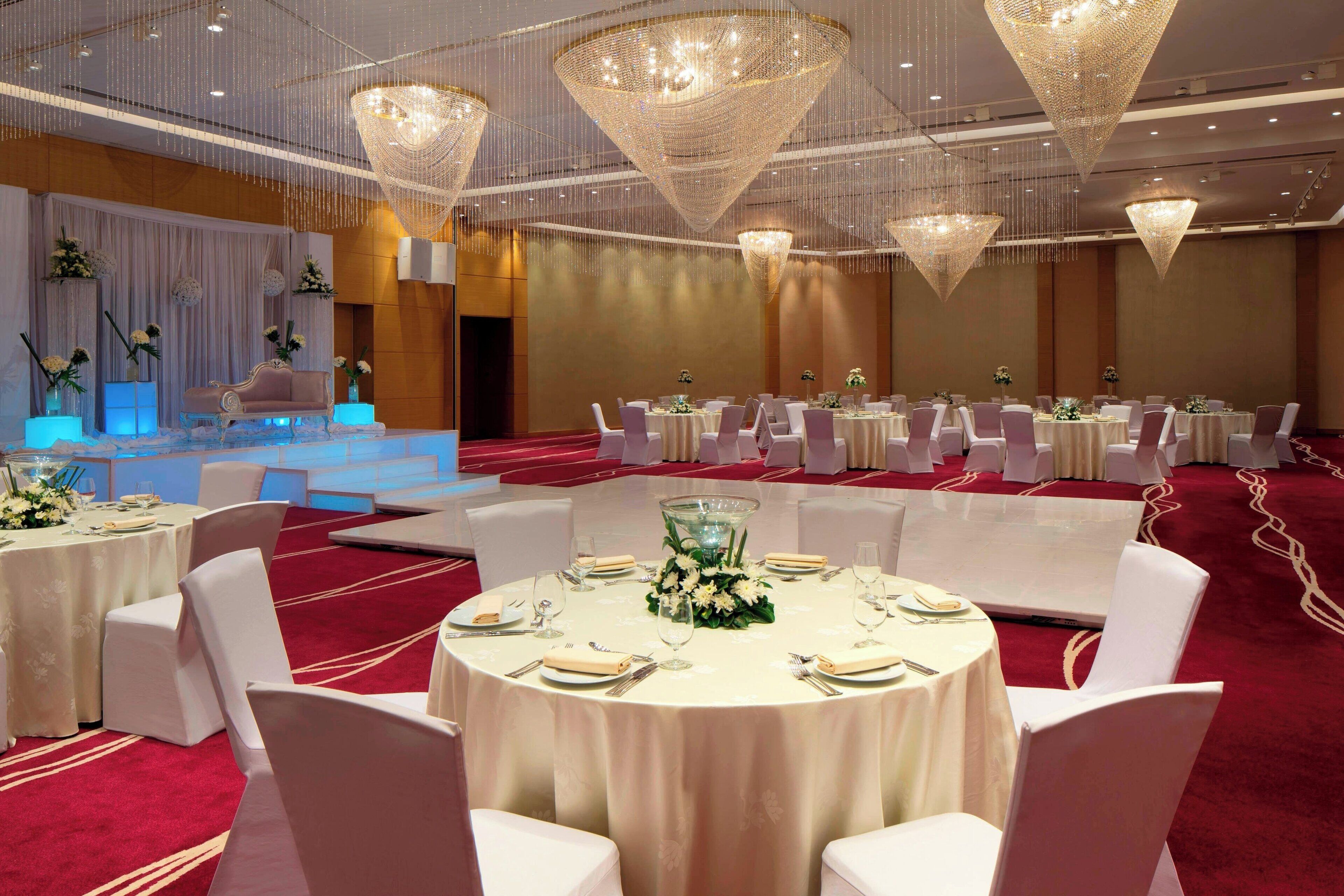 A banquet hall with round tables, white chairs, and hanging chandeliers.