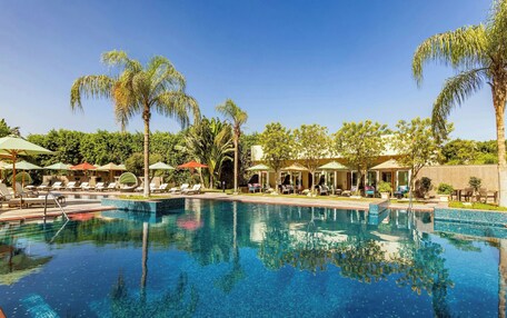 A swimming pool with lounge chairs and umbrellas, surrounded by palm trees and greenery.