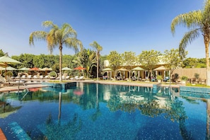 A swimming pool with lounge chairs and umbrellas, surrounded by palm trees and greenery. - Le Méridien Cairo Airport (Cairo)