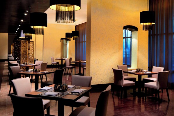 A restaurant with multiple tables and chairs, large hanging lamps, and a warm interior ambiance. - Le Méridien Cairo Airport (Cairo)
