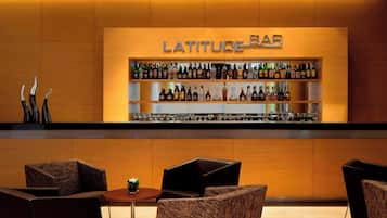 A bar area with a sign reading "LATITUDE BAR" and shelves stocked with various bottles. There are seating areas with chairs and a small table with a plant.