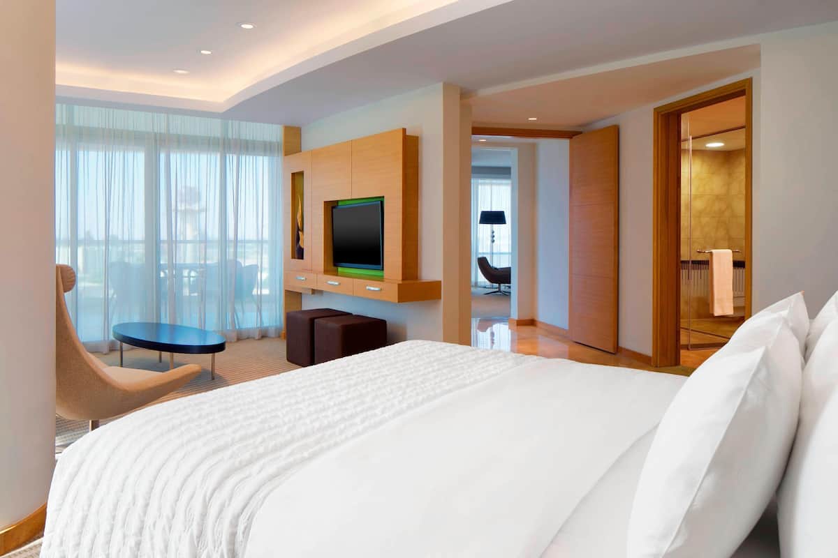 Une chambre d’hôtel avec un grand lit, un téléviseur fixé au mur, un coin salon avec un fauteuil et une petite table, et une vue par la fenêtre.