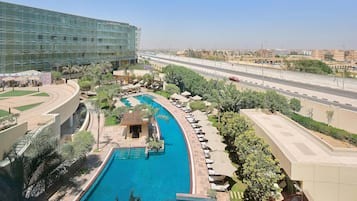 A hotel with a swimming pool, lounge areas, and a view of a highway.