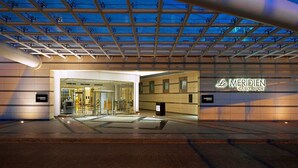 Entrada de hotel con fachada de vidrio, cartel de Le Meridien Cairo Airport y un paseo techado.