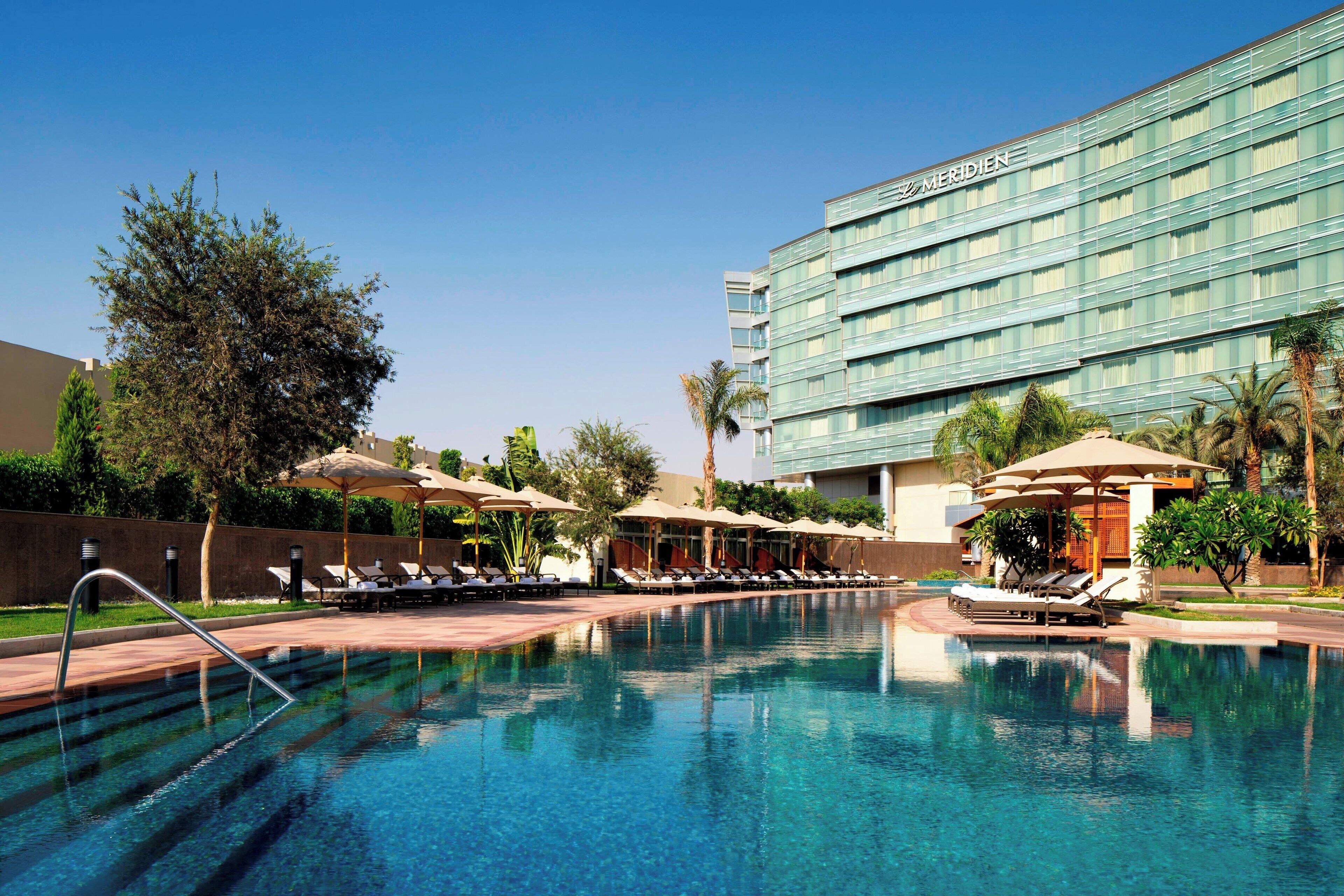 A swimming pool with lounge chairs and umbrellas, surrounded by a hotel building with the name 'Meridian'.
