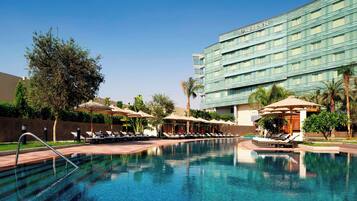A swimming pool with lounge chairs and umbrellas, surrounded by a hotel building with the name 'Meridian'.