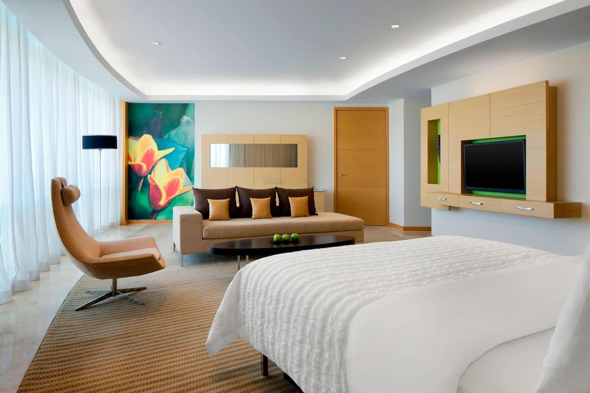Une chambre d’hôtel moderne, dotée d’un grand lit, d’un canapé, d’un fauteuil, d’un téléviseur à écran plat et d’un tableau au mur.