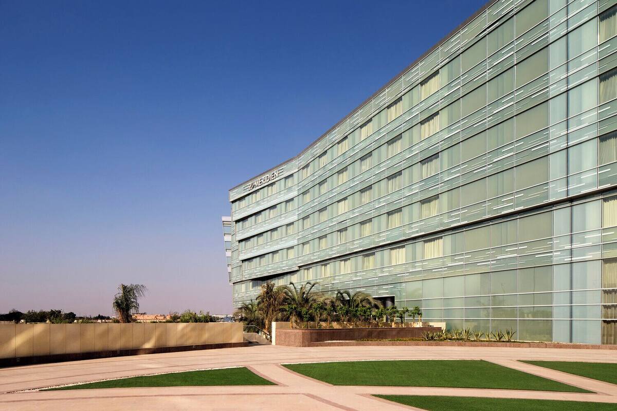 Un bâtiment moderne à la façade vitrée, portant l’inscription « MERIDIAN », et doté d’une cour aménagée avec des allées et de la verdure.
