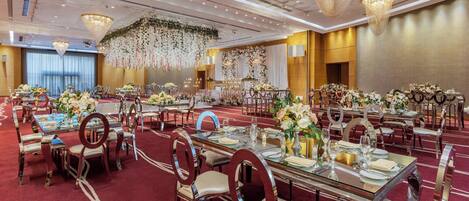 A banquet hall with multiple round tables, each set with chairs and floral centerpieces.