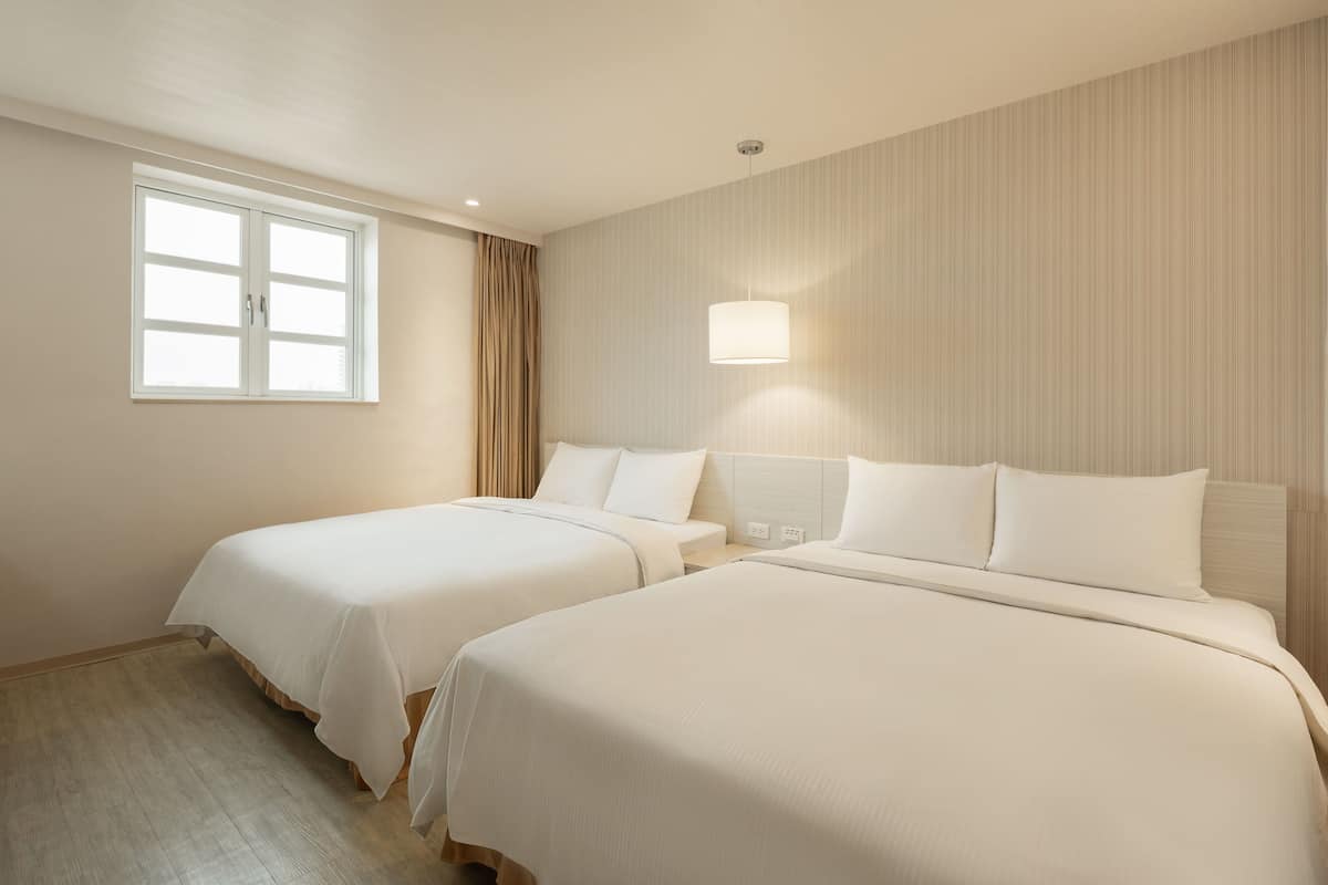 Een hotelkamer met twee bedden, een raam, een wandlamp en een houten vloer.