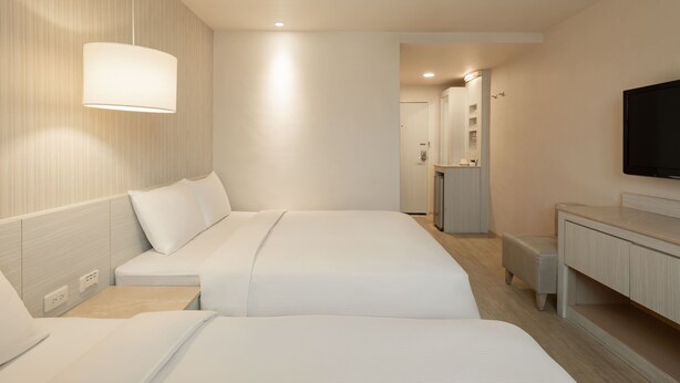 Une chambre d’hôtel moderne équipée de deux lits, d’une télévision à écran plat, d’une coiffeuse avec un miroir et d’un petit coin salon.