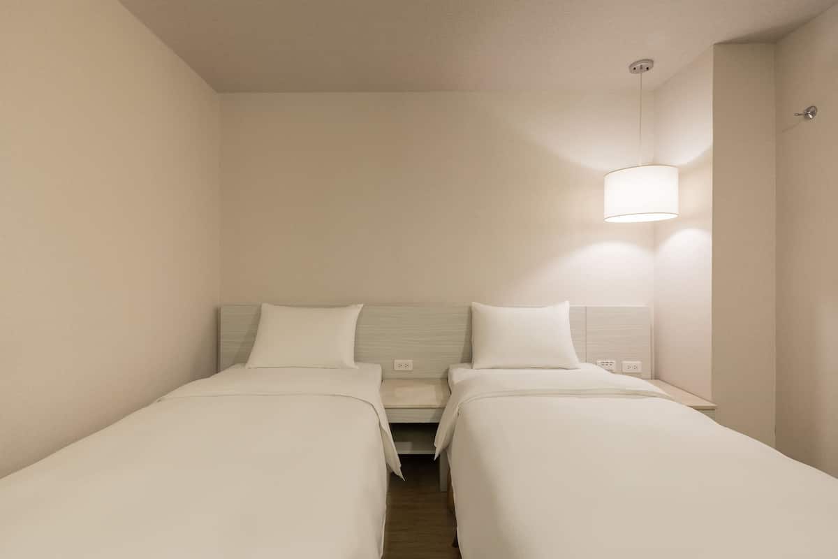 Een kleine, schone kamer met twee enkele bedden, een nachtkastje, een lamp en een deur.