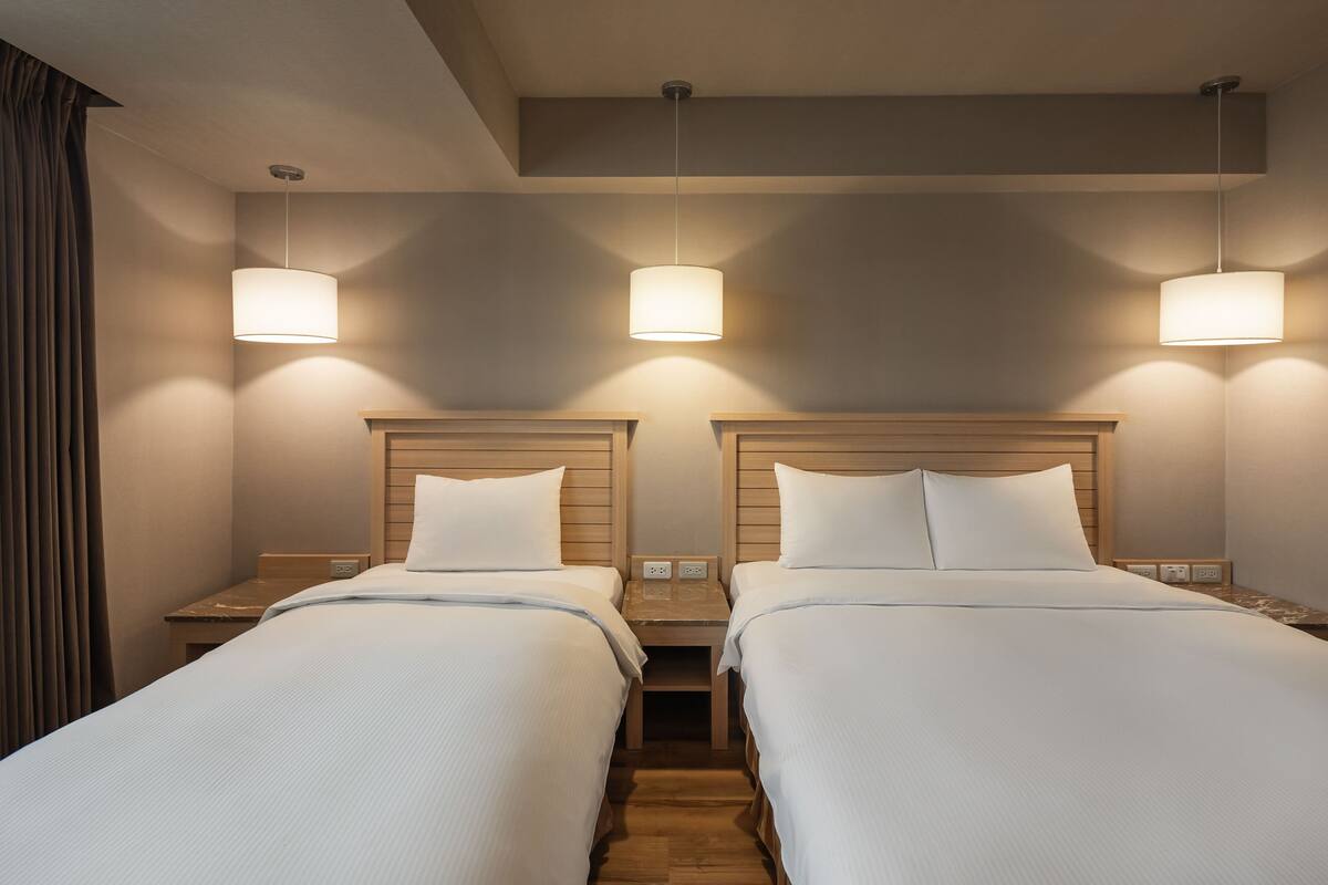 Une chambre d’hôtel avec deux lits, des têtes de lit en bois, des tables de chevet et des lampes suspendues.