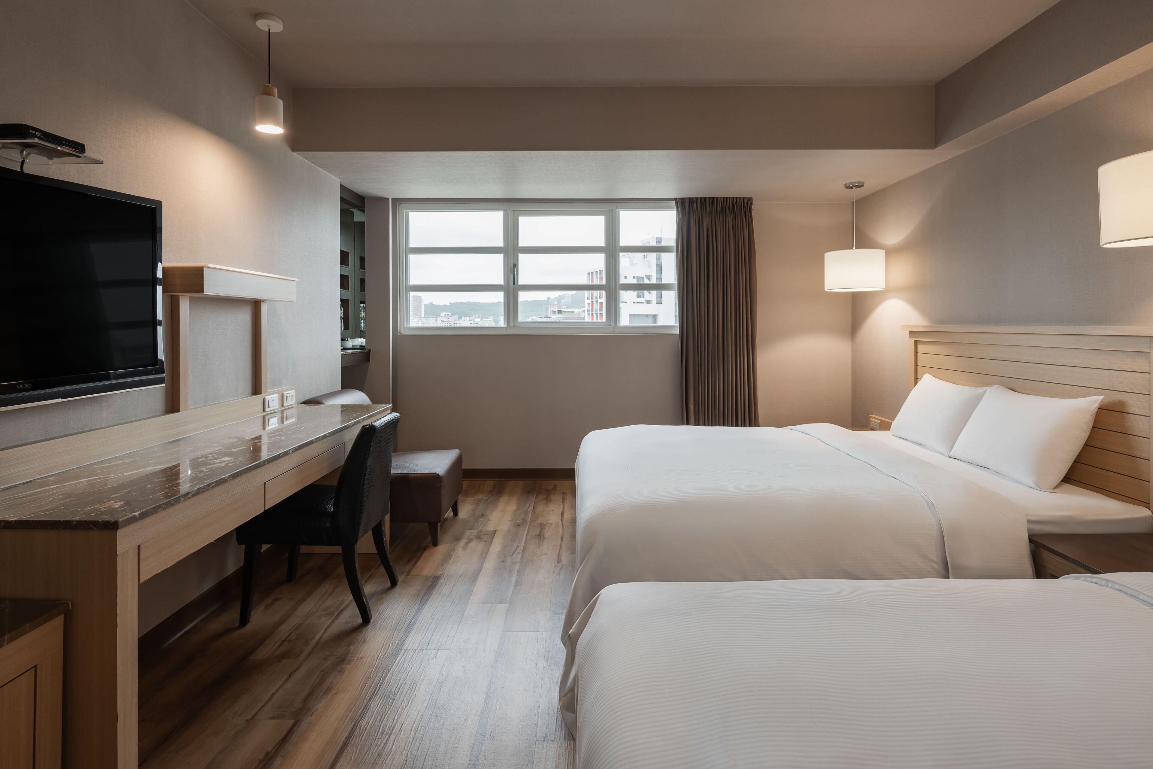 Una camera d'albergo con un letto, una scrivania, una sedia, una televisione e una finestra con tende.