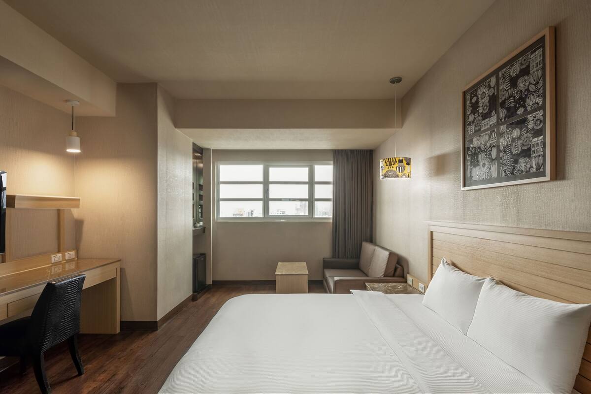 Une chambre d’hôtel avec un grand lit, un bureau, une chaise, une petite table et une fenêtre.