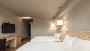 Een hotelkamer met twee bedden, een bureau, een televisie en een lamp.