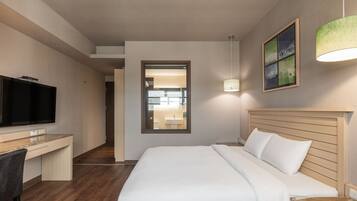 A hotel room with a bed, a desk, a television, and a bathroom visible through a door.