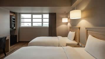 A hotel room with two beds, a desk, a chair, and a window with a view of the city.