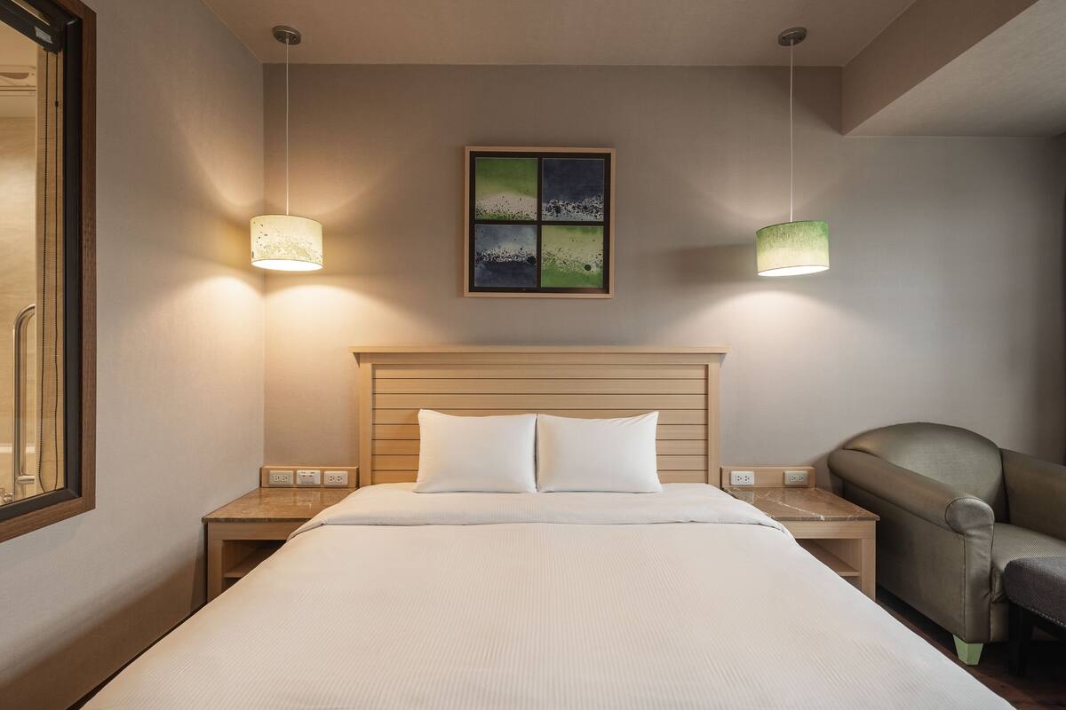 Une chambre d’hôtel avec un grand lit, deux tables de chevet, une chaise et une œuvre d’art accrochée au mur.
