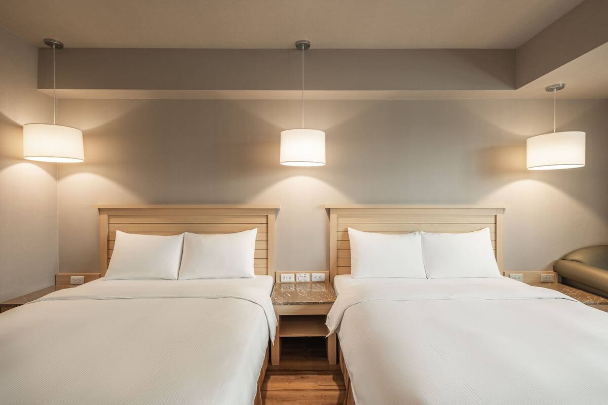 Une chambre d’hôtel avec deux lits, des têtes de lit en bois et une table de chevet avec une lampe.