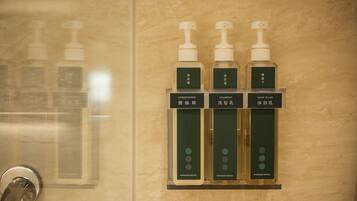 Un baño con cabina de ducha de vidrio y repisa con tres botellas de champú, acondicionador y gel de baño.